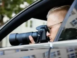 A man in a car with a telephone lens on his camera.