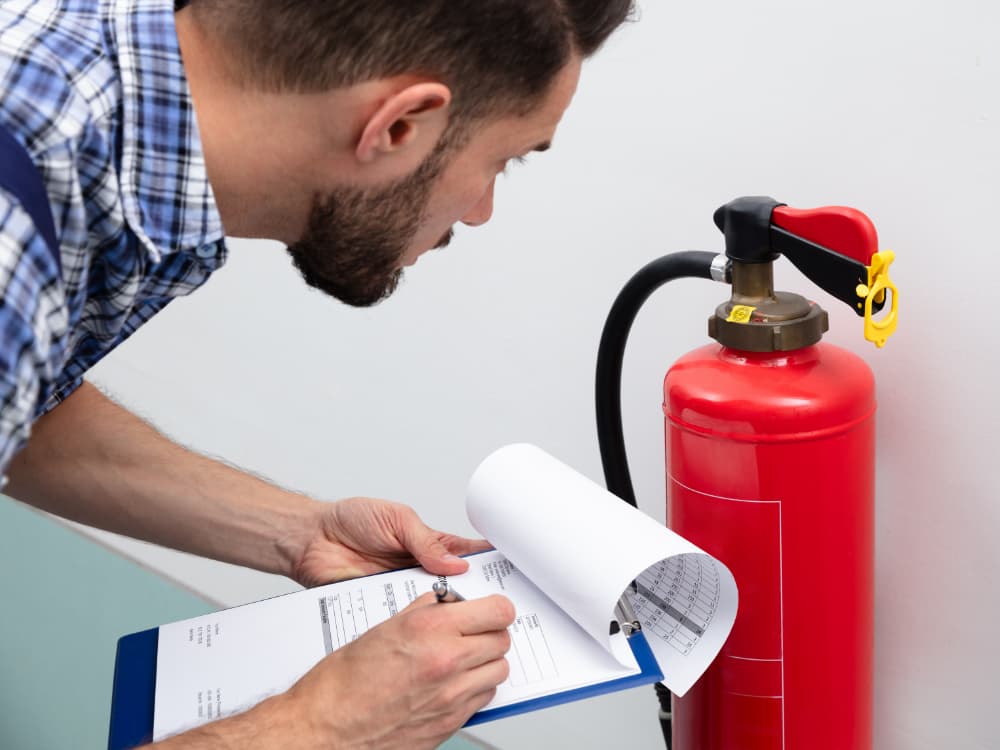 A man inspecting a fire extinguisher and making notes on a clipboard.